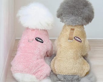 Könnte beinhalten: Zwei kleine Hunde tragen passende rosa und beige Plüsch-Hundeoutfits. Die Outfits haben ein Geschirrdesign mit einem kleinen Aufnäher mit der Aufschrift "DoDoPet". Die Hunde sitzen auf einer hellen Oberfläche.