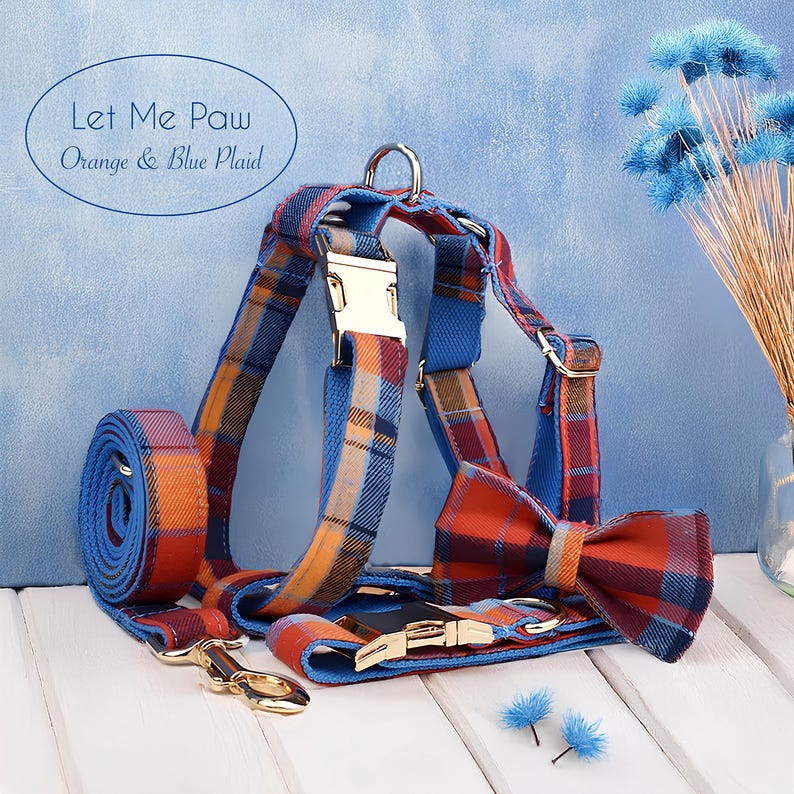 May include: A dog harness and matching bow tie set in orange and blue plaid. The set includes a leash, harness, and bow tie. The text "Let Me Paw Orange & Blue Plaid" is in a blue oval. The hardware is gold-colored.