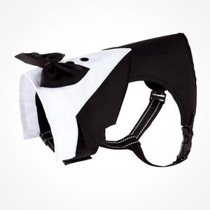 A black and white dog harness with a tuxedo-style bow tie. The harness has adjustable straps and a buckle closure.