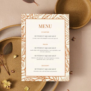 May include: A menu card with a floral design border in orange. The menu features butternut squash soup as a starter, main course, and dessert. The text is in a brown font.