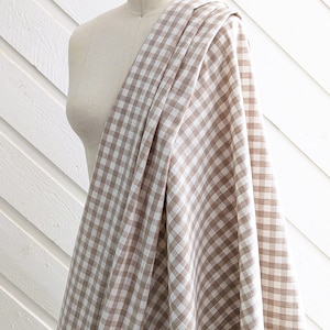 May include: A brown and white gingham fabric with a small check pattern. The fabric is draped over a dress form.