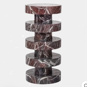 May include: A decorative marble side table with a stacked design. The table is made of dark red marble with white veining. The table is composed of several circular tiers of varying sizes.
