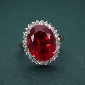 Op de afbeelding: Een ring met een rode edelsteen met een halo-setting van diamanten. De ring is van goud en heeft een grote ovale rode edelsteen in het midden.