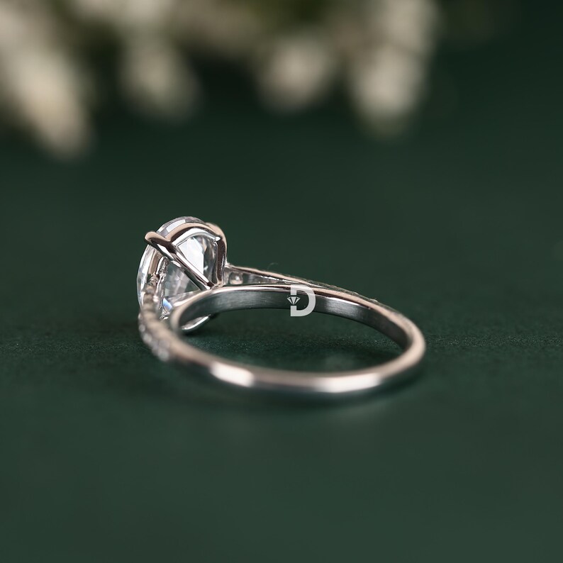 Embellished with Moissanite accent stones, this vintage-inspired engagement ring sparkles from every angle. These delicate accents are carefully set to enhance the brilliance of the centerpiece while maintaining a harmonious and balanced look. The intricate detailing and filigree work elevate the ring's artistry, giving it an authentic vintage appeal.