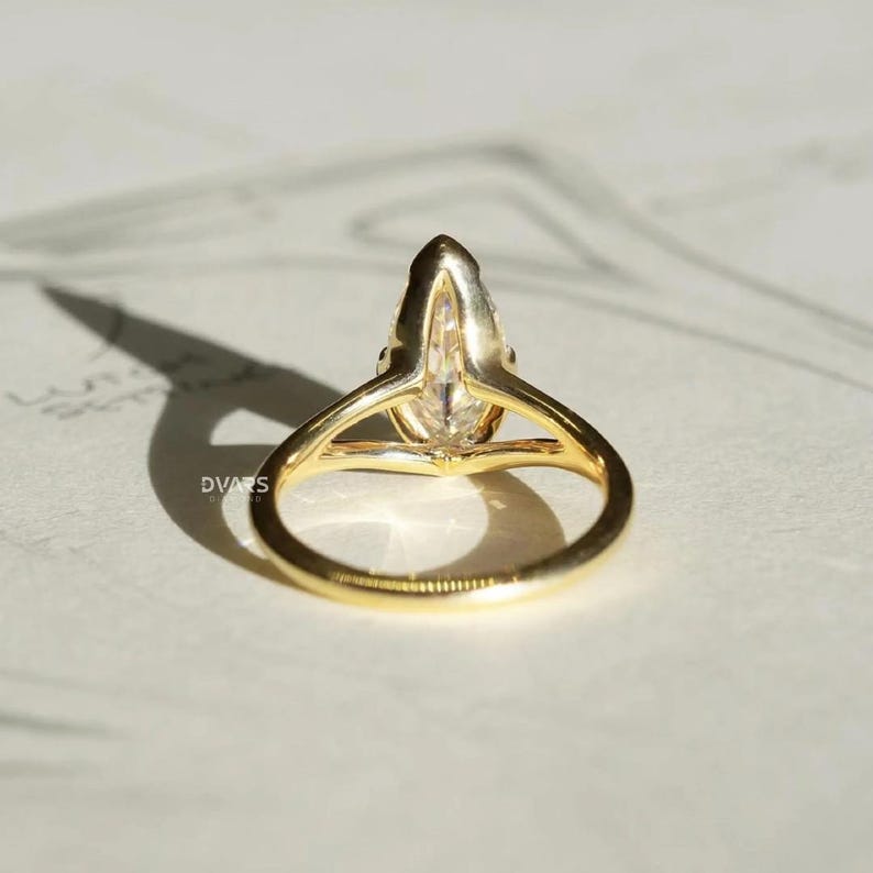 Pu&ograve; includere: Un anello d'oro con una gemma trasparente a forma di pera. La fascia dell'anello &egrave; in oro lucido e la gemma &egrave; incastonata in una delicata montatura a griffe. L'anello &egrave; mostrato da una prospettiva bassa, evidenziando la forma della gemma e il design dell'anello.