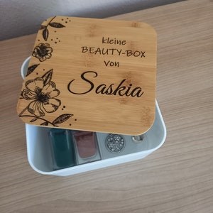Könnte beinhalten: Eine kleine Holzkiste mit floralem Design und dem Text "kleine BEAUTY-BOX von Saskia". Die Kiste ist geöffnet und enthält zwei kleine Flaschen Nagellack und einen silbernen Anhänger.