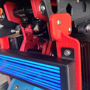 May include: A close-up of a black and red 3D printed part with a blue light bar. The part has a screw and a red knob. The text "FL" is visible on the part.