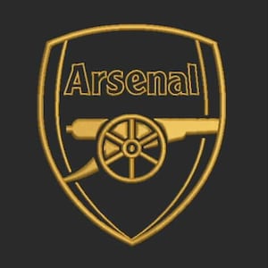 Puede incluir: Un escudo de fútbol del club Arsenal de color dorado con un cañón y la palabra "Arsenal" en forma de escudo.