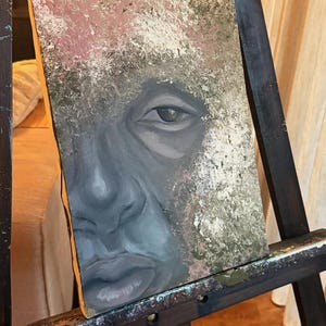 May include: A rectangular canvas painting featuring a close-up portrait of a face rendered in shades of gray, blue, and black. The surrounding area is textured with mottled layers of white, beige, and olive green paint, creating a contrast.