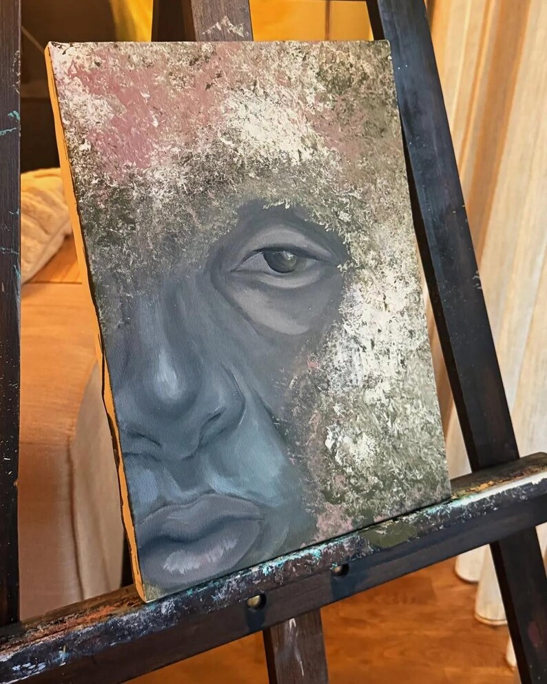 May include: A rectangular canvas painting featuring a close-up portrait of a face rendered in shades of gray, blue, and black. The surrounding area is textured with mottled layers of white, beige, and olive green paint, creating a contrast.