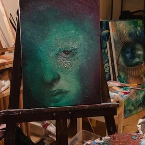 Puede incluir: Un cuadro rectangular sobre lienzo que presenta un retrato texturizado de un rostro en tonos verdes monocrom&aacute;ticos. La obra muestra sombras profundas, un ojo prominente y gruesas capas de pintura que crean una superficie rugosa.