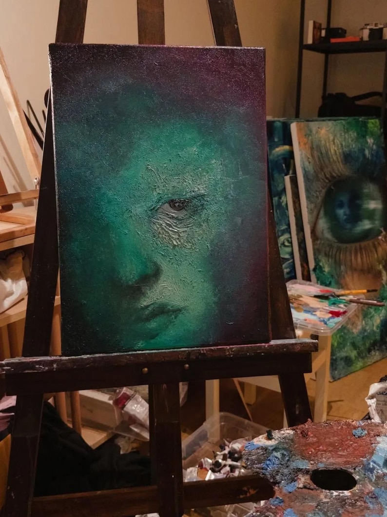 Puede incluir: Un cuadro rectangular sobre lienzo que presenta un retrato texturizado de un rostro en tonos verdes monocrom&aacute;ticos. La obra muestra sombras profundas, un ojo prominente y gruesas capas de pintura que crean una superficie rugosa.