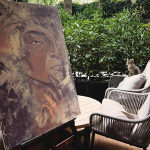 May include: A rectangular canvas painting on a black easel featuring a portrait of a person with a hand near their chin, rendered in shades of brown, gold, and dark purple with textured brushstrokes and visible paint layers.