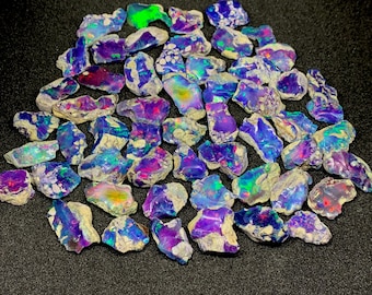 May include: A collection of raw opal gemstones, displaying a vibrant array of colors including blue, purple, green, and red. The opals have a rough, natural texture and are scattered across a dark surface.