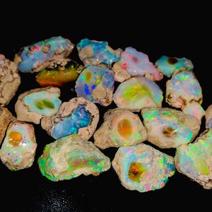 Peut inclure: Une collection de pierres précieuses d'opale brute dans différentes nuances de bleu, vert et blanc avec des reflets irisés de couleur. Les opales sont serties dans une matrice de roche gris foncé.