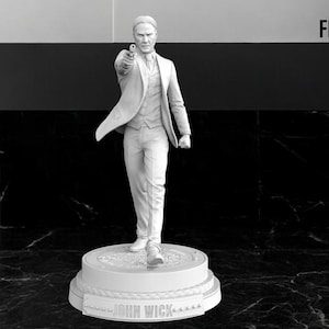 May include: A monochrome figurine of a man in a suit, holding a gun and pointing forward. The figurine is standing on a round base with the words "JOHN WICK" inscribed. The background is a dark marble pattern.