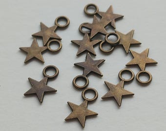 Könnte beinhalten: Eine Ansammlung kleiner, fünfzackiger Sternanhänger aus antik bronzefarbenem Metall. Jeder Stern verfügt über einen kreisförmigen Verbindungsring, der an einer der Spitzen befestigt ist und das Anbringen an Schmuckstücken ermöglicht.