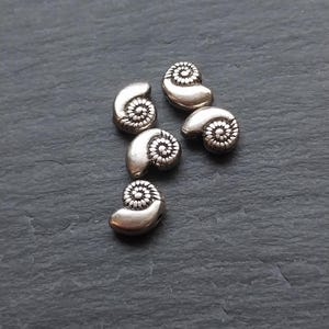 May include: Six silver-toned metal beads shaped like seashells with a raised spiral design.