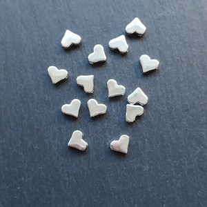 May include: A scattering of silver heart-shaped charms on a dark gray surface.