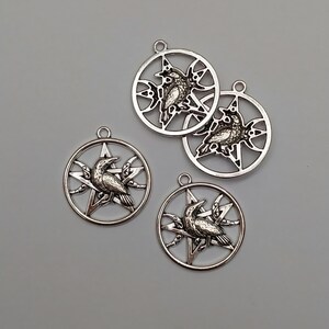 May include: Four circular silver-toned metal pendants, each featuring a central five-pointed star design with a detailed raven perched upon it. Each pendant includes a small loop at the top for attachment, showcasing a metallic finish.