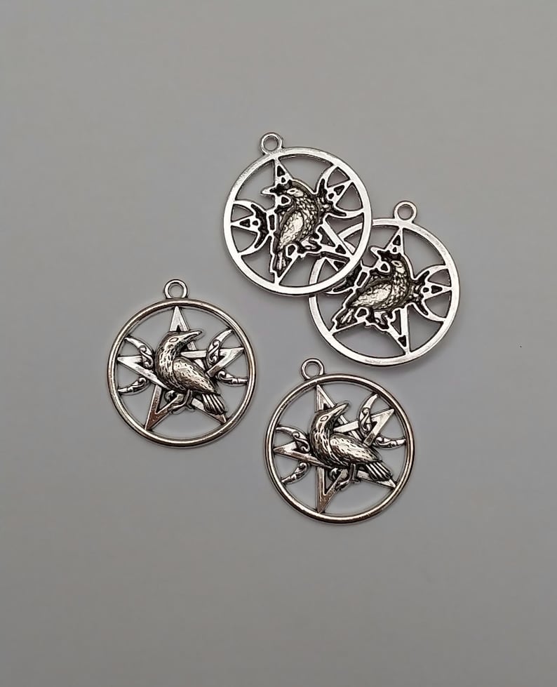 May include: Four circular silver-toned metal pendants, each featuring a central five-pointed star design with a detailed raven perched upon it. Each pendant includes a small loop at the top for attachment, showcasing a metallic finish.