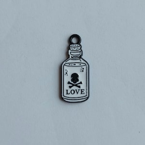 May include: A black and white bottle-shaped charm featuring a skull and crossbones symbol. The word "LOVE" is printed below the skull. The charm has a black loop at the top.