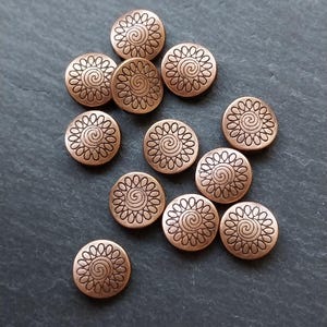 May include: A group of 12 copper-colored metal buttons with a swirl design. The buttons are round and have a raised design.