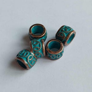 Puede incluir: Cinco cuentas metálicas de color turquesa y bronce. Cada cuenta tiene forma cilíndrica con un patrón detallado de espirales y puntos. Las cuentas tienen un aspecto envejecido y antiguo, con el color turquesa visible en las zonas hundidas.