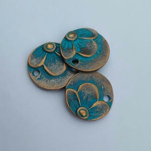 Puede incluir: Tres cuentas redondas de metal con un diseño floral turquesa y bronce. Cada cuenta tiene un pequeño agujero para ensartar. Las cuentas tienen un acabado envejecido, lo que les da un aspecto vintage.