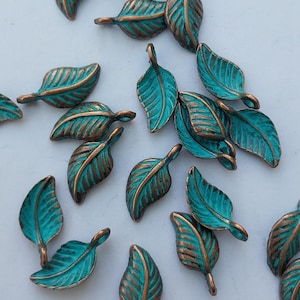 Peut inclure: Collection de breloques en forme de feuilles de couleur turquoise et bronze. Chaque feuille pr&eacute;sente un motif de veines d&eacute;taill&eacute; et une boucle pour l'attacher &agrave; des bijoux ou autres cr&eacute;ations. Les feuilles sont &eacute;parpill&eacute;es sur une surface blanche.