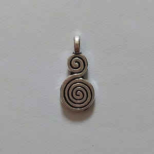 Pode incluir: Um pingente prateado com um design em espiral. O pingente apresenta duas espirais sobrepostas, cada uma com círculos concêntricos, e uma pequena argola no topo para uma corrente. O pingente é provavelmente feito de metal.