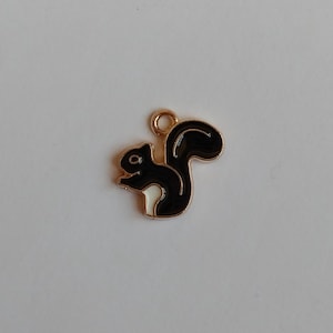 Peut inclure: Une petite breloque en forme d'écureuil avec un contour en métal doré, remplie d'émail noir brillant et dotée d'une touche blanche sur le bas du corps. La breloque comprend un anneau de jonction circulaire au sommet pour la fixation.