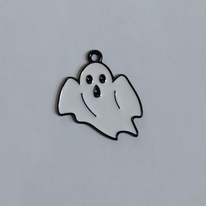 Peut inclure: Un charm en émail blanc en forme de fantôme avec des contours noirs. Le fantôme présente deux yeux ronds noirs et une bouche noire de forme ovale. Une petite boucle circulaire est positionnée au centre supérieur pour la fixation.
