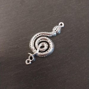 May include: Silver-toned metal snake charm with a coiled body and a detailed design. The charm has a loop at the top for attaching to a necklace or bracelet.