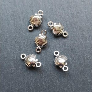May include: Five silver-toned metal shell-shaped charms with two jump rings each. The charms are designed to be used for jewellery making.