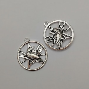 May include: Two silver-toned metal circular pendants, each featuring a five-pointed star design with a central raven figure. Each pendant includes a small loop at the top for attachment, showcasing intricate cut-out details and a metallic finish.