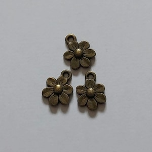 May include: Three bronze-colored daisy flower charms with a loop at the top for jewelry making. Each flower has detailed petals and a central disc. The charms are on a white background.