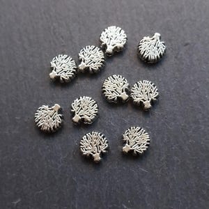 May include: A collection of silver-toned metal charms shaped like trees. The charms are small and round, with intricate details.