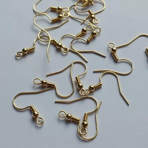 May include: A collection of gold-toned metal earring hooks, each featuring a small decorative bead and a coiled spring detail at the base of the wire. These jewellery findings are designed with a curved ear wire and a small loop for attaching charms.