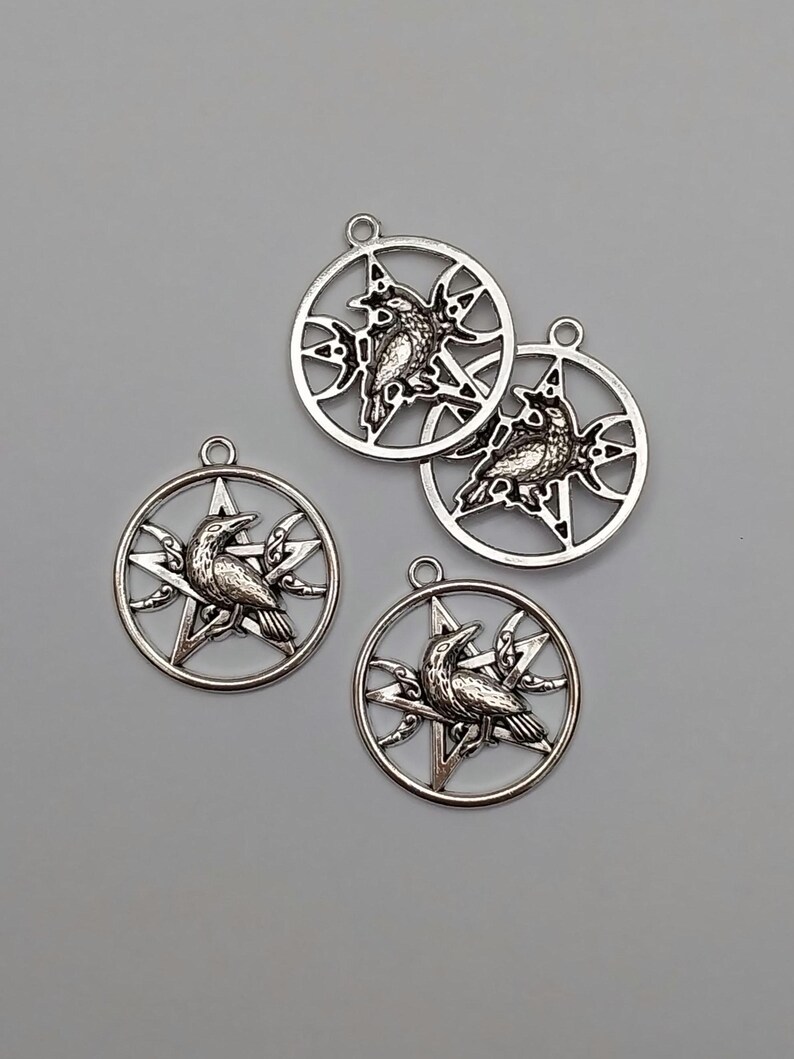 May include: Four silver-toned metal pendants, each featuring a circular frame enclosing a five-pointed star and a crescent moon. A detailed raven is depicted perched in the center of each star. Each pendant includes a small loop at the top.