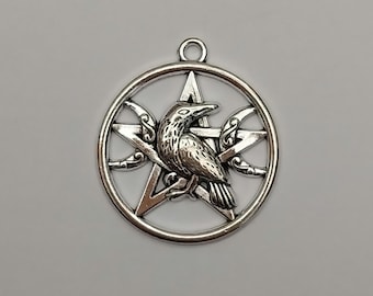 Op de afbeelding: Een ronde, zilverkleurige metalen hanger met een vijfpuntig sterontwerp in het midden. Een gedetailleerde raaf bevindt zich in het centrum van de ster, geflankeerd door twee maansikkels aan weerszijden. De hanger heeft een klein oogje.