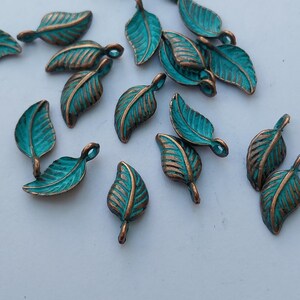 Peut inclure: Plusieurs petits charmes en forme de feuilles de couleur turquoise, avec des veines et des bords de couleur bronze. Ces breloques en m&eacute;tal sont dispers&eacute;es sur une surface blanche, mettant en valeur leur design d&eacute;taill&eacute; et leur finition rustique. Id&eacute;al pour le bricolage.