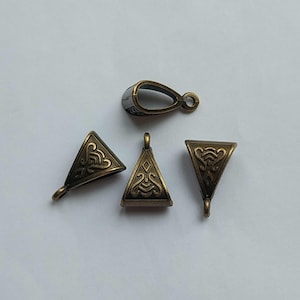 May include: Four antique bronze-toned metal jewelry bails, each featuring a triangular shape with an embossed decorative pattern. Three bails are oriented vertically with a small loop at the top, while one bail is positioned horizontally.