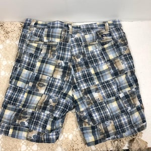 May include: Blue, yellow, and white plaid shorts with a patchwork design. The shorts have pockets and a button closure. The brand name "Chaps" is visible on the back pocket. These shorts are a casual summer garment.