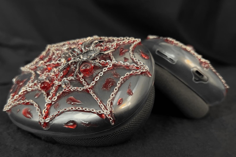 May include: A pair of black wireless headphones with a spiderweb design. The headphones are decorated with silver chains and red beads.