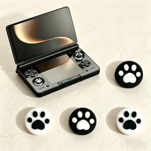 Pode incluir: Console de jogos portátil preta com tela aberta. Possui vários botões e um direcional. Quatro protetores de polegar com pegadas pretas e brancas também são visíveis.