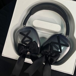Puede incluir: Un par de auriculares negros con un acabado degradado gris y negro. Los auriculares tienen lazos negros en cada auricular.
