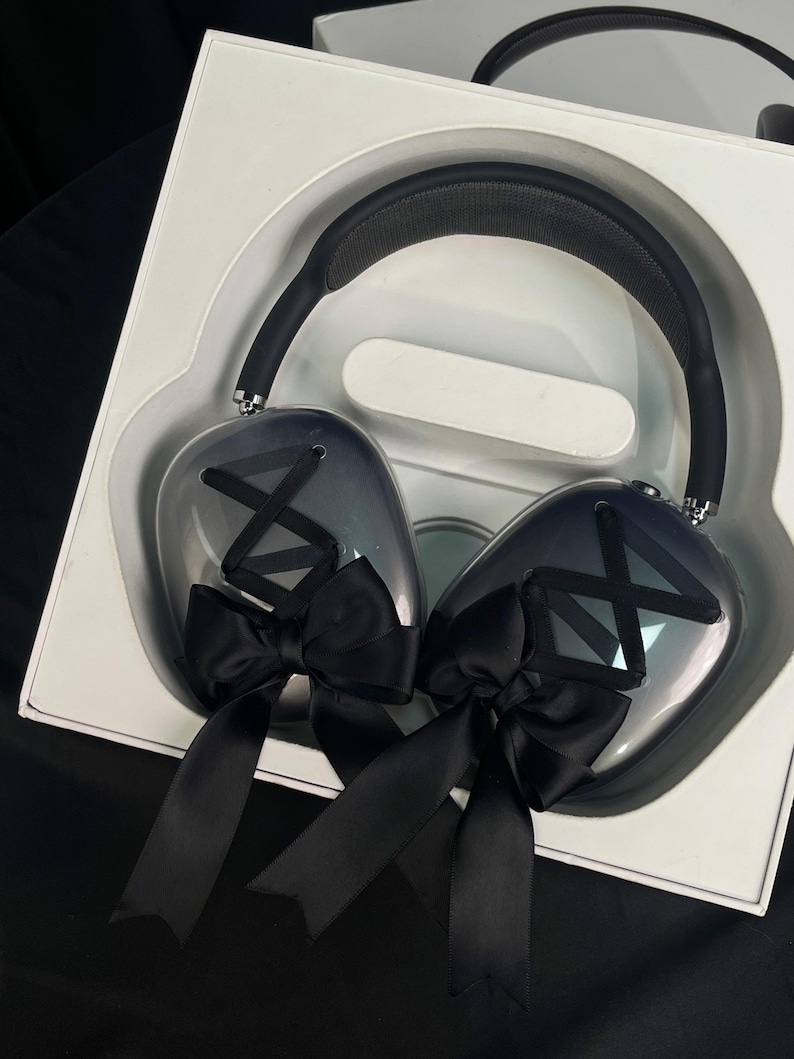 Puede incluir: Un par de auriculares negros con un acabado degradado gris y negro. Los auriculares tienen lazos negros en cada auricular.