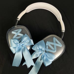 Puede incluir: Auriculares de diadema blancos con auriculares de pl&aacute;stico transparente decorados con lazos de sat&eacute;n azul.