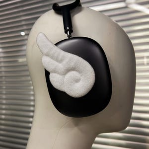 May include: Black over-ear headphones with a white, textured wing design attached to the ear cup. The headphones are on a mannequin head. The headband and ear cup are black.